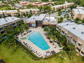 Eine Vogelperspektive auf ein Hotel mit Swimmingpool, Liegestühlen und Palmen.