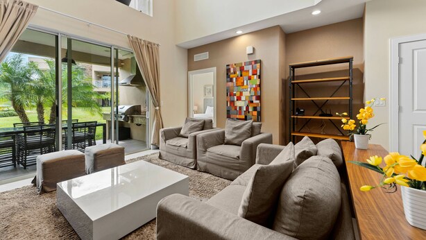 A spacious living area with a large sofa set, a coffee table, and a wooden side table with yellow flowers. - 7648 Magic Village 8 guests 4 suites 8 min Disney  (Kissimmee)