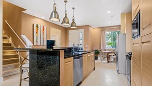 A modern kitchen with a central island, stainless steel appliances, wooden cabinets, and pendant lighting. - 7648 Magic Village 8 guests 4 suites 8 min Disney  (Kissimmee)