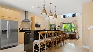A modern kitchen with a stainless steel refrigerator, wooden cabinets, and a central island with bar stools. - 7648 Magic Village 8 guests 4 suites 8 min Disney  (Kissimmee)