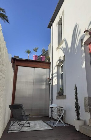 A small outdoor patio with a metal gate, a folding chair, a small table, and potted plants.