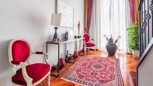 Una habitación con una silla roja, una consola con lámpara, una alfombra grande y una planta en maceta.