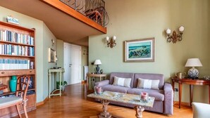 Una sala de estar con piso de madera, un sofá morado, una mesa de centro, una estantería y un cuadro en la pared.