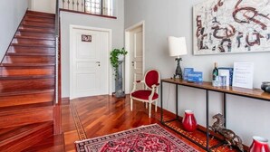 Una escalera que lleva al segundo piso, una silla roja, una mesa con una lámpara y un cuadro abstracto grande en la pared.