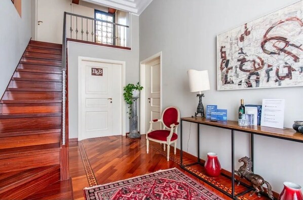 A staircase leading to a second floor, a red chair, a table with a lamp, and a large abstract painting on the wall.