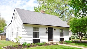 A white single-story house with a black door and windows, number 163, surrounded by a well-maintained lawn and small garden. - Charming Home In Quiet Location Near Downtown Holland! (Holland)