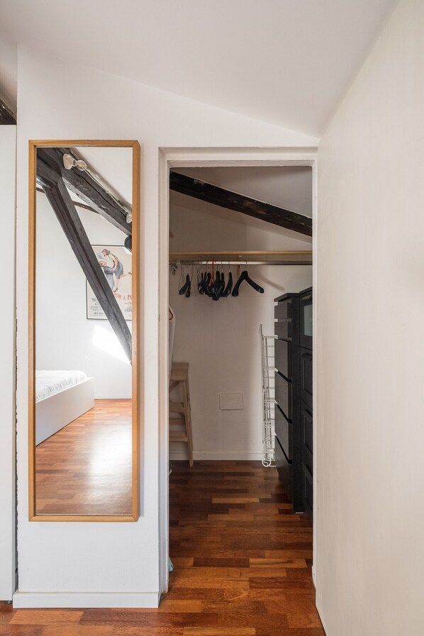 Un corridoio con pavimento in legno, un appendiabiti con abiti appesi e una scala con ringhiera in legno.
