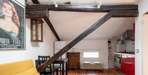 Eine Loft-Wohnung mit freiliegenden Holzbalken, einer Küche mit roten Schränken und einem Essbereich mit gelber Couch.