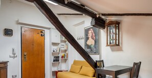 Ein Zimmer mit Holzboden, einer Couch, einem Tisch mit Stühlen, einer Holzkommode, einer Uhr und einem Poster an der Wand.