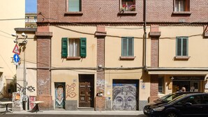 A two-story building with a brick facade, green shutters, and a mural on the ground floor.