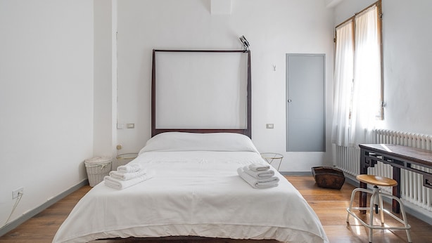 A minimalist bedroom with a large bed, a wooden floor, a radiator, and a window with curtains.