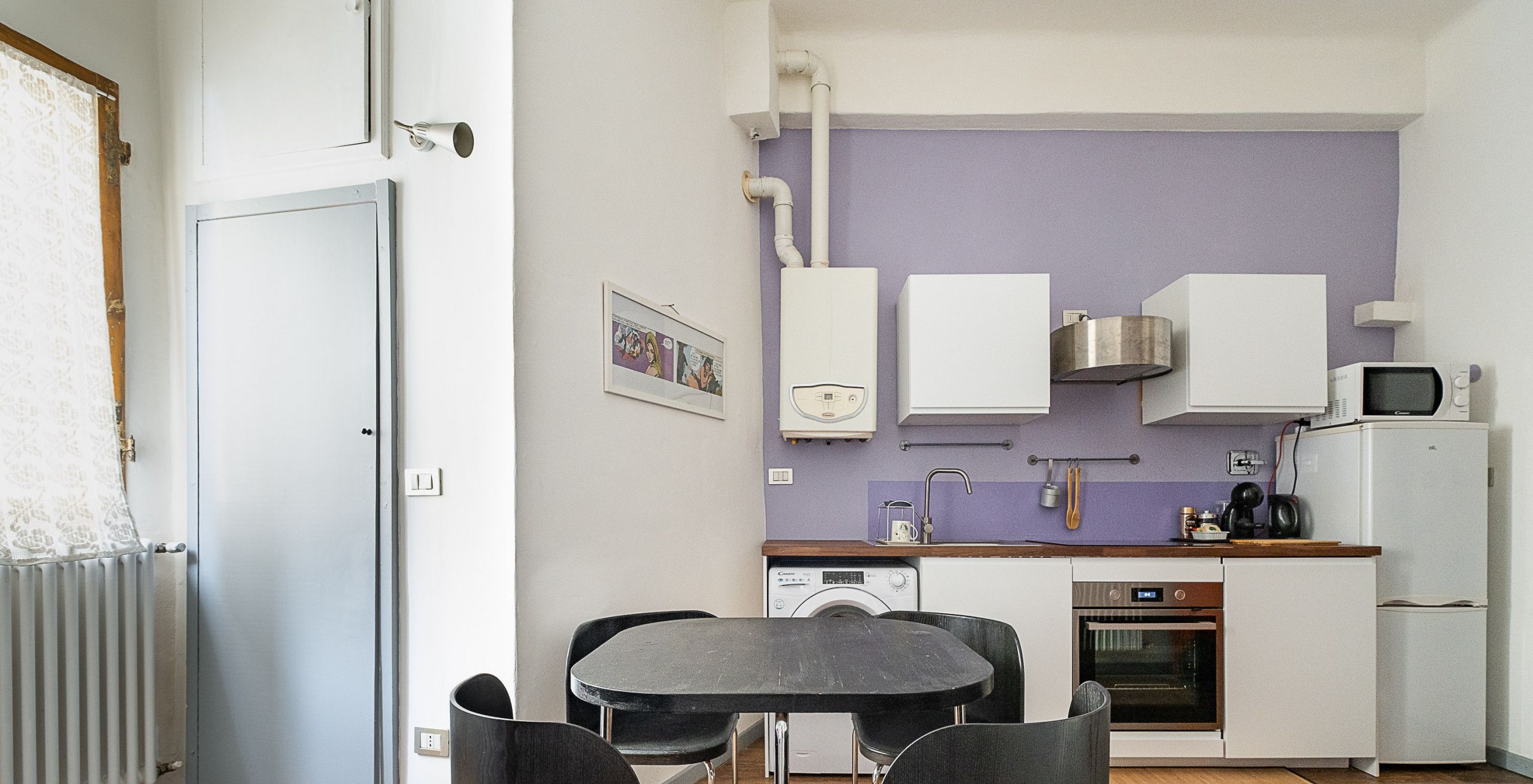 Cocina compacta con electrodomésticos modernos, comedor con mesa y sillas, y calentador de agua a la vista.