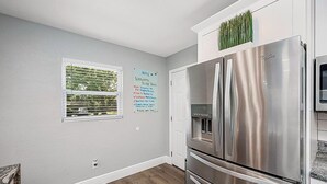 Een keuken met een roestvrijstalen koelkast, een raam met zonwering en een welkomstbord aan de muur.