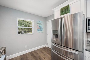 A kitchen with a stainless steel refrigerator, a window with blinds, and a welcome sign on the wall.