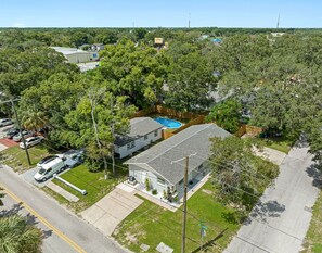 A residential area with a house featuring a swimming pool, surrounded by trees and a street.
