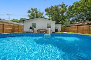 A swimming pool with a wooden deck, a house with a porch, and a wooden fence.