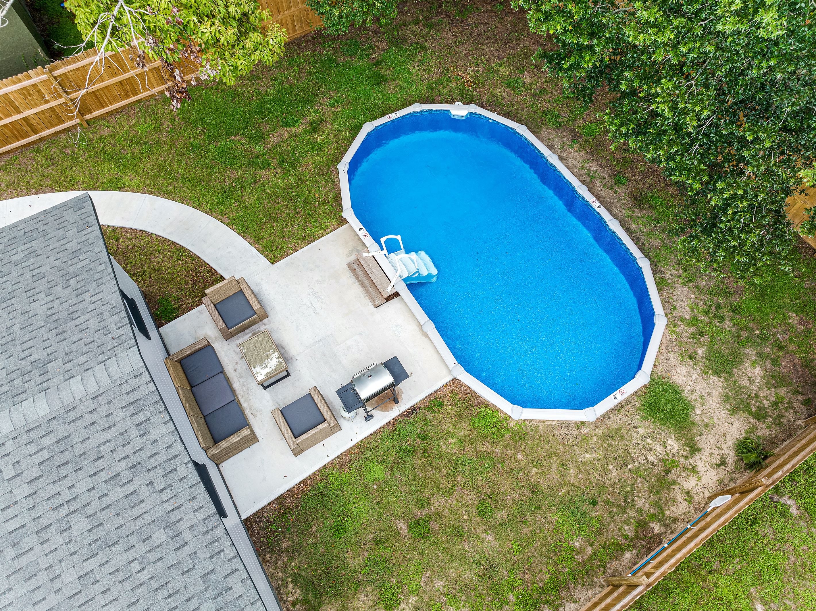 Eine Vogelperspektive zeigt einen Garten mit Swimmingpool, Terrassenmöbeln und einer Holzterrasse.