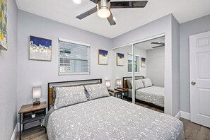 A bedroom with a bed, bedside tables, a ceiling fan, a large mirror, and artwork on the walls.