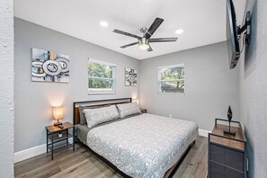 A bedroom with a bed, bedside tables, a ceiling fan, and artwork on the walls.