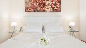 Ett hotellrum med en stor säng, vita sängkläder, två sängbord med lampor och en blomstermålning på väggen.