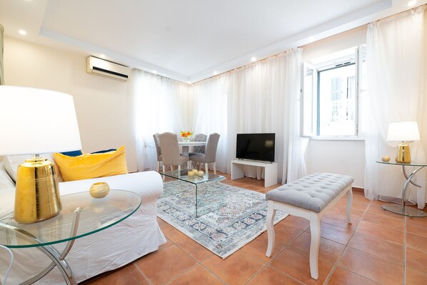 A modern hotel room with a glass coffee table, a sofa, a TV, and a small dining table. - Nadiona White Suite | Elegant Guilford Apartment | old Town center (Kerkira)