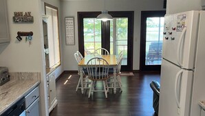 Una cocina con mesa y sillas, refrigerador y ventana con persianas.
