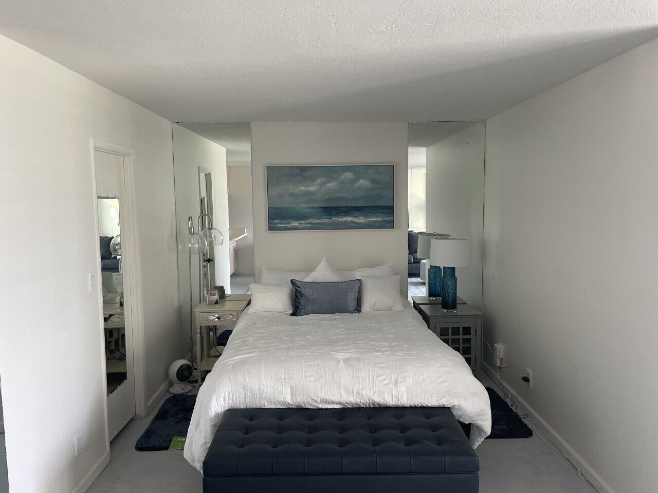 A modern bedroom with a large bed, a bedside table, a mirror, and a painting of a landscape.
