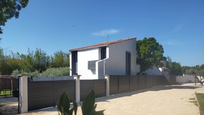 Ein modernes Haus mit weißer Fassade und rotem Dach, umgeben von einem Holzzaun und viel Grün.
