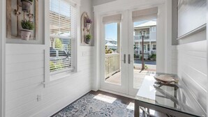 A hallway with white walls, a glass table, and a view of a deck and houses outside.
