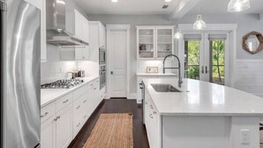 A modern kitchen with white cabinetry, stainless steel appliances, and pendant lighting.