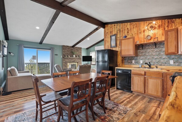 Une cuisine moderne avec des meubles en bois, un coin repas avec une table et des chaises en bois, et une vue sur l’extérieur grâce à de grandes fenêtres.