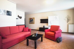 A living room with a red sofa, a red armchair, a black coffee table with a laptop, and artwork on the walls. - "Villa Imelda" spacious, bright apartments, garden or balcony, lake view (Limone Sul Garda)