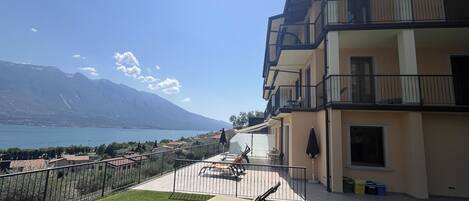 A balcony with a view of a lake and mountains, outdoor furniture, and a building with balconies.