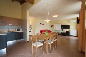 A modern kitchen with a microwave, a dining table with chairs, a red sofa, and a wall-mounted air conditioner. - "Villa Imelda" spacious, bright apartments, garden or balcony, lake view (Limone Sul Garda)