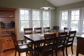 A dining room with a wooden table and chairs, large windows, and a ceiling light fixture. - Heated POOL thru October!  Professionally redone, fantastic location in Dewey! (Dewey Beach)