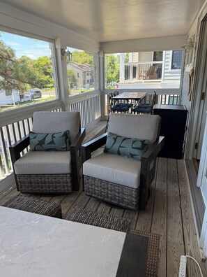 A covered porch with wicker furniture, a table, and a view of the street.