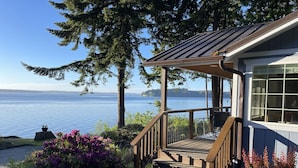 A wooden deck with a railing leading to a covered porch overlooking a body of water.