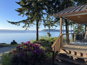 A wooden deck with outdoor furniture overlooking a lake, surrounded by trees and shrubs.