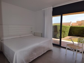 Un dormitorio con una cama grande, una silla y vistas a un jardín a través de una puerta corrediza de vidrio.