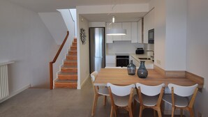 Eine moderne Küche mit weißen Schränken, einem Edelstahlkühlschrank und einer Essecke mit einem Holztisch und weißen Stühlen.