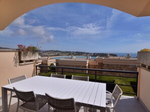 Una terraza con mesa y sillas blancas, con vistas a la costa, edificios y una playa.