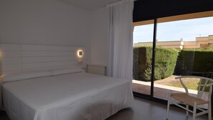 Ein modernes Schlafzimmer mit einem großen Bett, einem Sessel und Blick auf einen Garten durch eine Schiebetür.