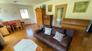 A living room with a brown leather sofa, a wooden coffee table, and a patterned rug. There is a dining area with a red table and striped chairs. A wooden cabinet and a globe are on a shelf above the sofa. - Baiersbronn, Black Forest, Schwarzwald, view, 2 rooms, sun, balcony, quietness (Baiersbronn)