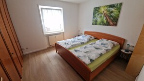 A bedroom with a wooden bed, a window with curtains, a radiator, and a wall-mounted painting.