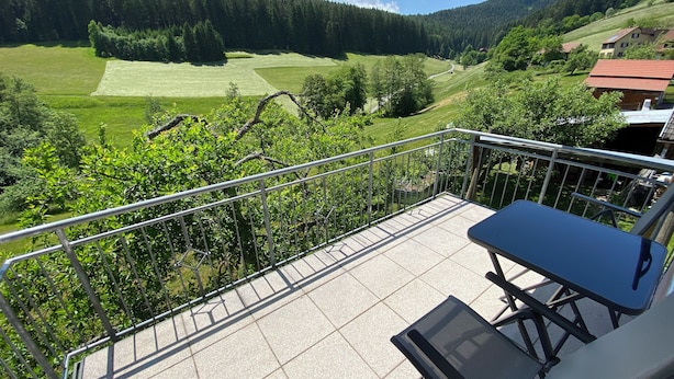 A balcony with a table and chairs, overlooking a green landscape with trees and a road. - Baiersbronn, Black Forest, Schwarzwald, view, 2 rooms, sun, balcony, quietness (Baiersbronn)