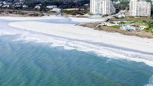 Eine Luftaufnahme einer Küstenregion mit Strand, einer Marina und mehreren Hochhäusern.
