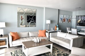 A modern living room with a white sofa, a coffee table, and a dining area with a table and chairs.