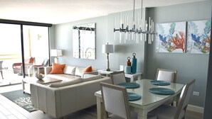 Ein modernes Wohnzimmer mit einer Couch, einem Esstisch und Stühlen. Eine Chandelier, Kunstwerke an den Wänden und eine Aussicht durch ein großes Fenster.