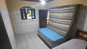 Un petit logement composé d’une seule pièce, comprenant un lit, une fenêtre et un ventilateur de plafond.