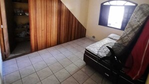 Un petit appartement d’une seule pièce, avec un plafond en pente, une fenêtre donnant sur un beau paysage, un lit, un ventilateur et un sol carrelé.